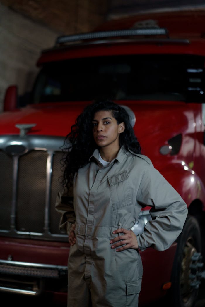 Black woman in gray uniform standing confidently by a red truck indoors.