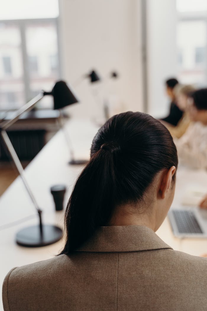 Back view of a professional woman working in a modern office setting with colleagues.
